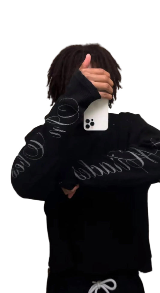 Person wearing a black hoodie with white text, holding a phone in front of their face.